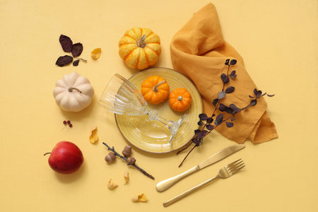 Beautiful table setting with fresh pumpkins, apple, acorns, branches and autumn leaves on yellow backgroundの写真素材