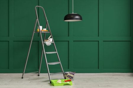 Stepladder with cans of paint and tools near green wall