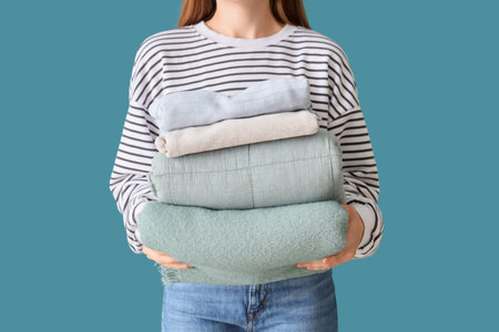 Young woman with stack of stylish clothes on blue background, closeupの写真素材