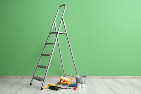 Stepladder with cans of paint and tools near green wallの写真素材