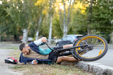 Young man fallen off his bike and lying on grass outdoorsの写真素材