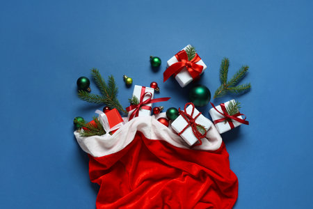 Santa bag with Christmas balls, gift boxes and fir branches on blue backgroundの写真素材