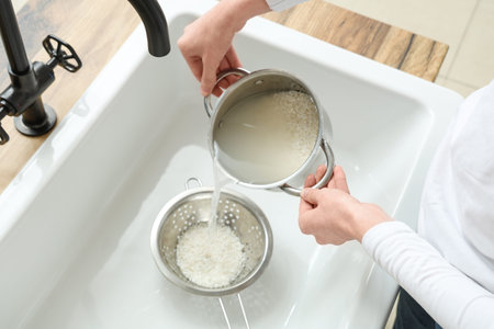 Woman rinsing rice with pot and sifter in sink, closeup