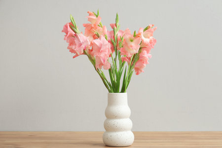 Vase with bouquet of beautiful gladiolus flowers on wooden table against white backgroundの写真素材