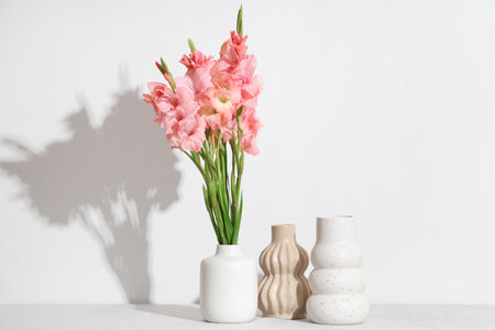 Vase with bouquet of beautiful gladiolus flowers on table against white backgroundの写真素材