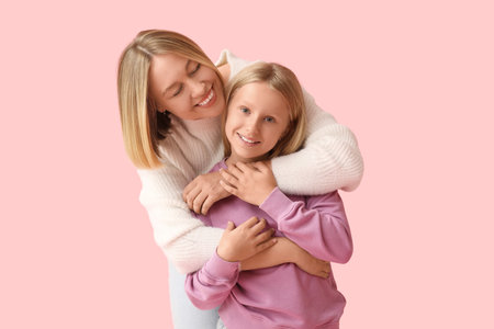 Beautiful woman hugging her cute daughter in stylish sweaters on pink backgroundの写真素材