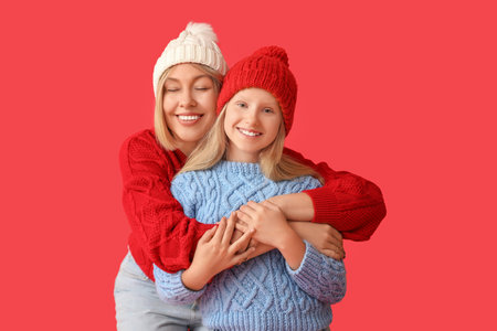 Beautiful woman with her cute daughter in sweaters and hats on red stylish backgroundの写真素材