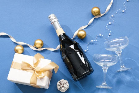 Bottle of champagne with glasses, gift box, pine cone and Christmas balls on blue backgroundの写真素材
