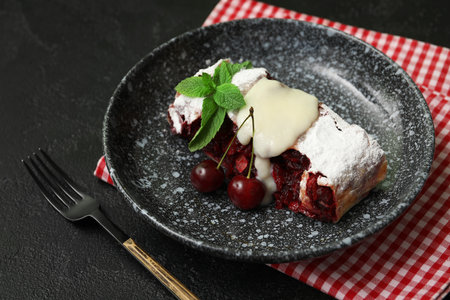 Plate with piece of tasty cherry strudel and napkin on black backgroundの写真素材
