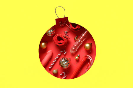 Christmas ball made of decorations and sex toys visible through hole on yellow background
