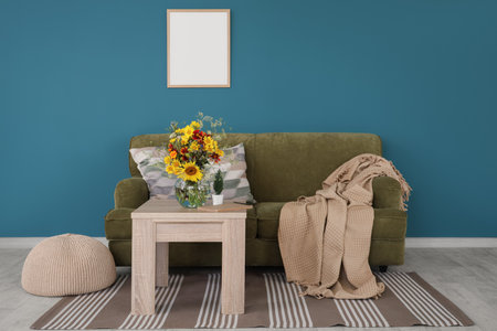 Cozy sofa with plaid and wild flowers in vase on coffee table in living roomの写真素材