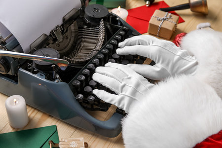 Santa Claus hands with Christmas decor typing on typewriter against beige wooden backgroundの写真素材