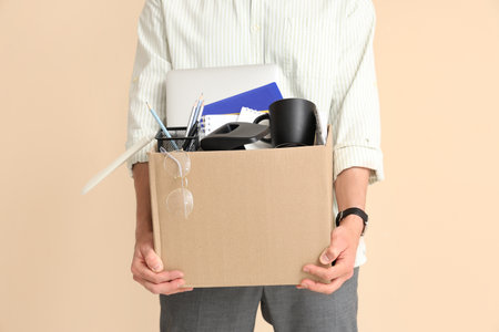 Fired young man holding box with personal stuff on beige background, closeupの写真素材