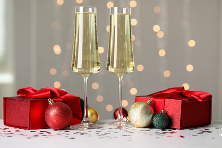 New Year composition with glasses of champagne, gift boxes and Christmas balls against blurred lightsの写真素材
