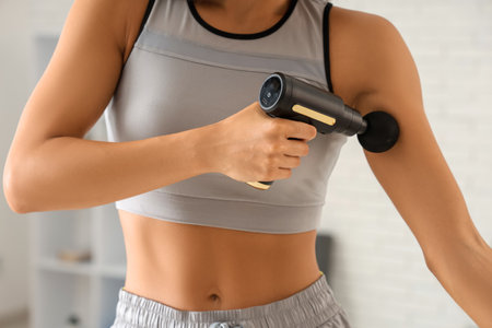Sporty young woman using percussive massage device after training in gym, closeupの写真素材