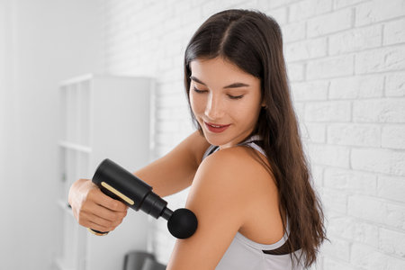 Sporty young woman using percussive massage device after training in gymの写真素材