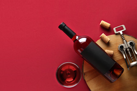 Wooden tray with bottle, glass of wine, corks and opener on red backgroundの写真素材