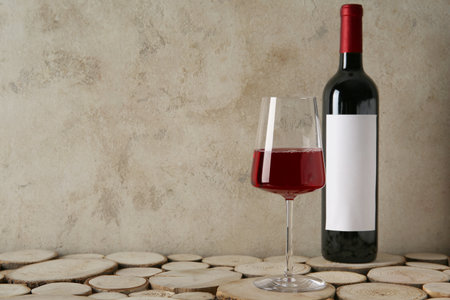 Bottle and glass of red wine on wooden table against grunge beige backgroundの写真素材