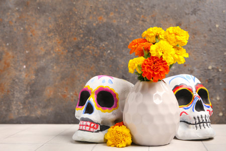 Vase with beautiful marigold flowers and painted human skulls on light tile table. El Dia de Muertosの写真素材