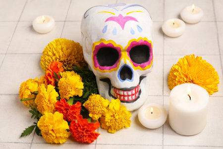 Painted human skull, marigold flowers and burning candles on light tile background. El Dia de Muertosの写真素材