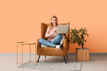Young beautiful woman sitting on armchair and using laptop at homeの写真素材