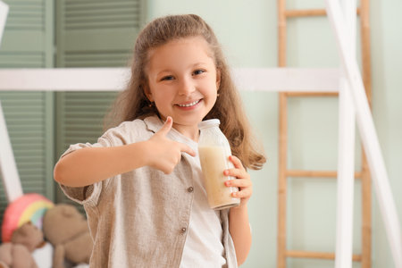 Happy little girl pointing at bottle of yogurt in roomの写真素材