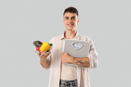 Young man with weight scales and vegetables on light backgroundの写真素材