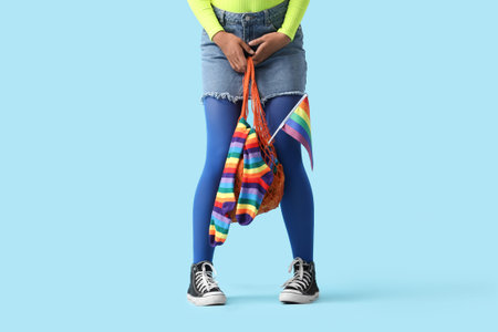 Young woman holding string bag with LGBT flag and rainbow stockings on blue background