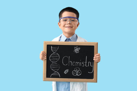 Cute little boy in lab coat holding chalkboard with text CHEMISTRY on blue background