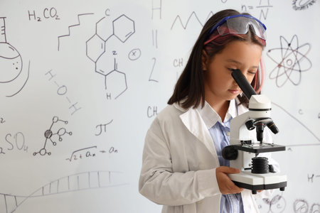 Cute little girl using microscope in chemistry classroom