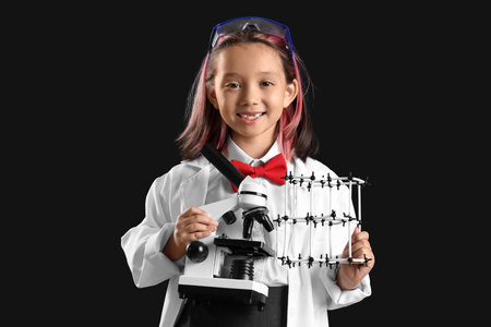 Cute little girl holding microscope and molecular model on black backgroundの写真素材