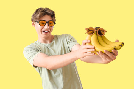 Young man in sunglasses with bananas on yellow backgroundの写真素材