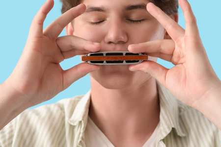 Young man playing harmonica on blue background, closeupの写真素材