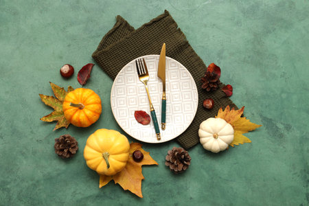 Beautiful table setting with autumn leaves, chestnuts, pine cones and fresh pumpkins on green backgroundの写真素材
