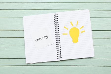 Notebook with word COACHING and light bulb on green wooden background