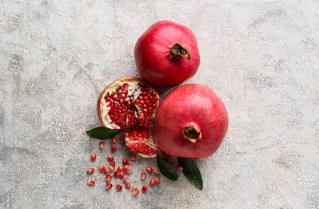 Fresh ripe pomegranates with seeds and leaves on gray backgroundの写真素材