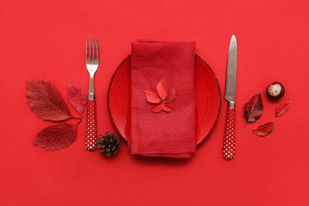 Beautiful table setting with pine cone, chestnut and autumn leaves on red backgroundの写真素材
