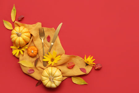 Stylish cutlery with fresh pumpkins, flowers and autumn leaves on red backgroundの写真素材