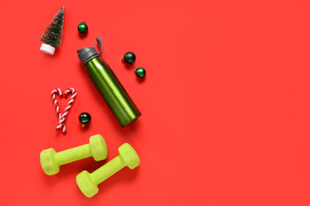 Composition with dumbbells, sports water bottle and Christmas decorations on red backgroundの写真素材