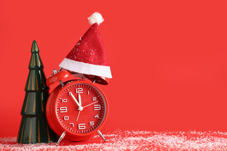 Alarm clock, Santa hat and ceramic Christmas tree on red backgroundの写真素材