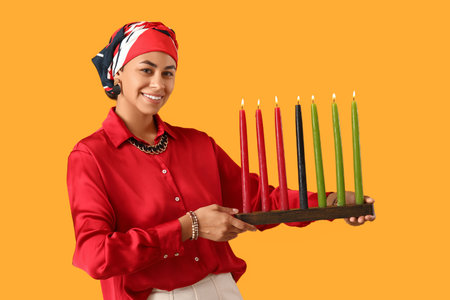 Young African-American woman with burning candles on yellow background. Kwanzaa celebrationの写真素材