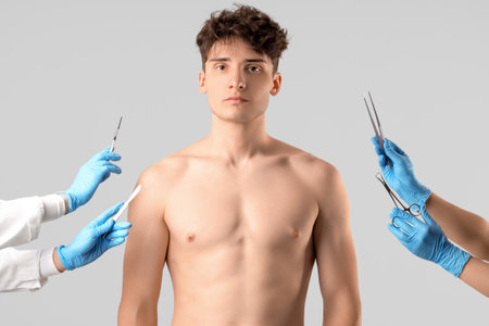 Young man and plastic surgeons with instruments on gray backgroundの写真素材