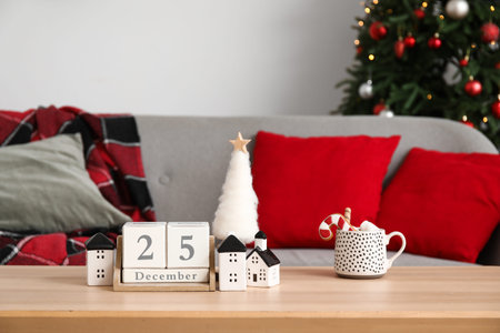 Cube calendar with date of Christmas, toy houses and cocoa on table in living room, closeup