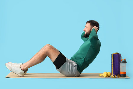 Sporty young man exercising on yoga mat against blue backgroundの写真素材
