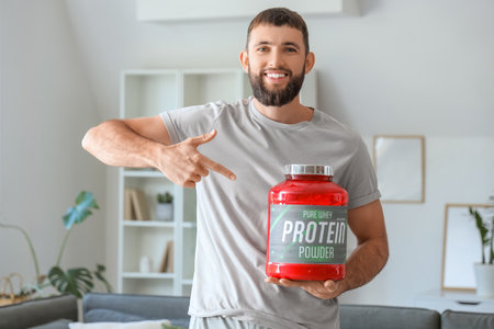 Sporty young man pointing at jar of protein powder at homeの写真素材