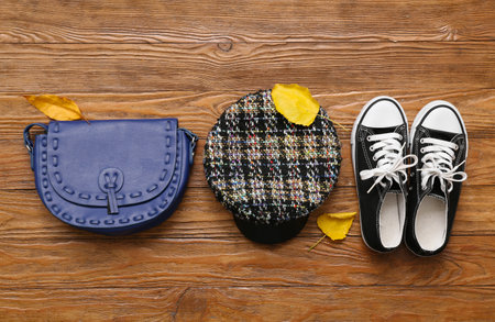 Stylish female bag with cap, shoes and autumn leaves on wooden backgroundの写真素材