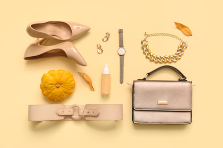 Stylish female bag with high heeled shoes, accessories and autumn decor on beige backgroundの写真素材