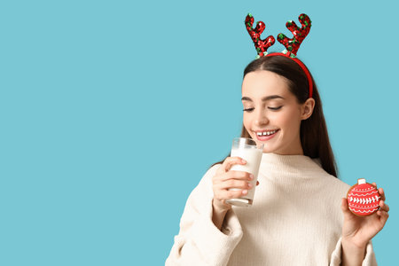 Young woman with tasty Christmas gingerbread cookie and milk on blue backgroundの写真素材