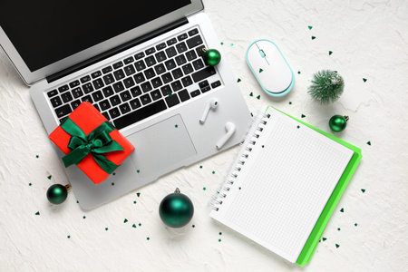 Laptop with notebook, gift and Christmas balls on white background