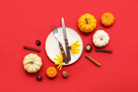 Beautiful table setting with fresh pumpkins, chestnuts, flowers, cinnamon and autumn leaves on red backgroundの写真素材